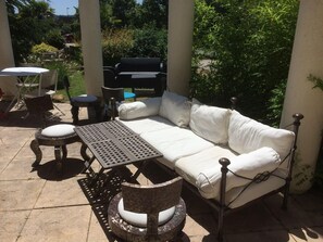 An outdoor patio area with a white cushioned sofa, two round tables, and wicker chairs. - Balladins Lyon Est (Saint-Quentin-Fallavier)