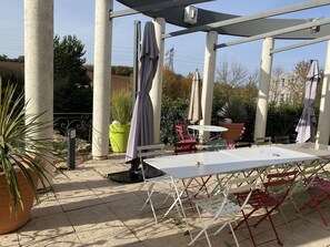 An outdoor patio with a white table and chairs, surrounded by potted plants and umbrellas. - Balladins Lyon Est (Saint-Quentin-Fallavier)