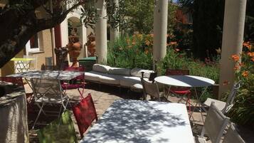 An outdoor patio area with tables and chairs, surrounded by plants and flowers.