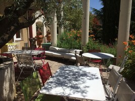 An outdoor patio area with tables and chairs, surrounded by plants and flowers.