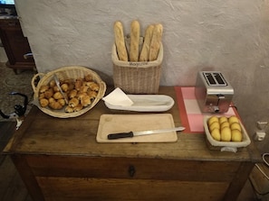 A wooden counter with a basket of croissants, a basket of baguettes, a cutting board with a knife, a toaster, and a tray of lemons. - Balladins Lyon Est (Saint-Quentin-Fallavier)