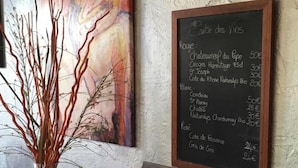 A chalkboard menu with wine and cheese prices, a painting, and a wooden sculpture on a table. - Balladins Lyon Est (Saint-Quentin-Fallavier)