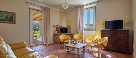Una sala de estar con sofá, chimenea, televisión y comedor con sillas.