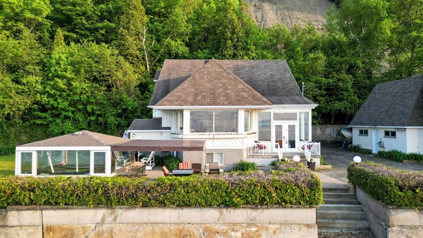 Une maison à deux étages dotée d’un patio couvert, d’un quai pour bateaux et offrant une vue sur une colline rocheuse.