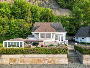 A two-story house with a covered patio area, a boat dock, and a view of a rocky hillside.
