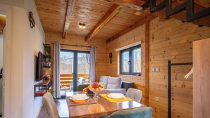 A wooden cabin interior with a dining table, chairs, a sofa, and a window.