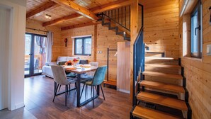 A wooden cabin interior with a dining area, a staircase, and a view of the outdoors.