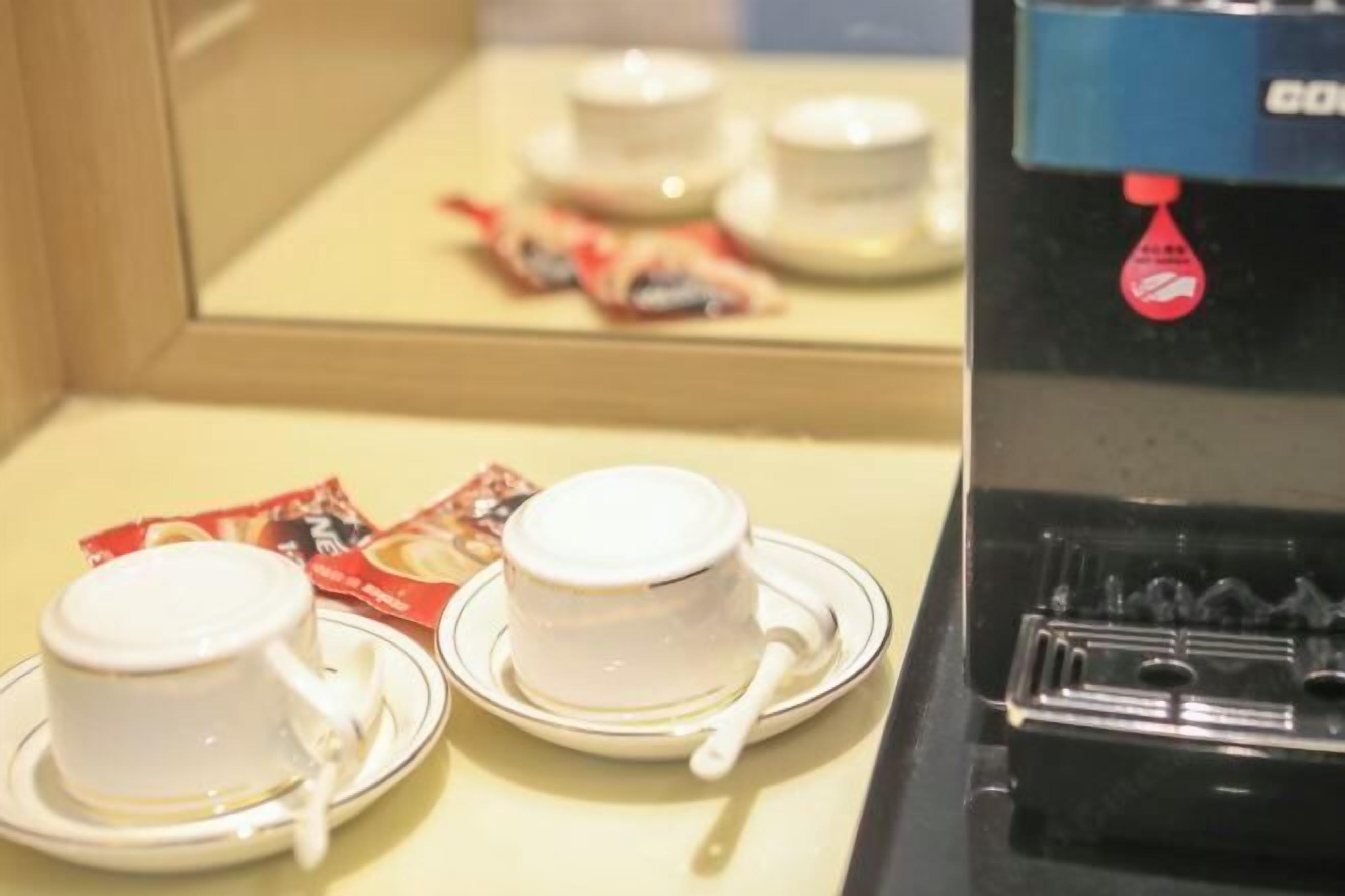 Due tazze bianche su sottopiatti con un cucchiaino, una bustina di tè e una macchina da caffè con un'etichetta rossa.