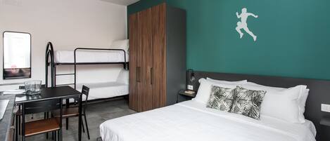 A hotel room with a bunk bed, a desk with a chair, a wardrobe, and a bed with white bedding.