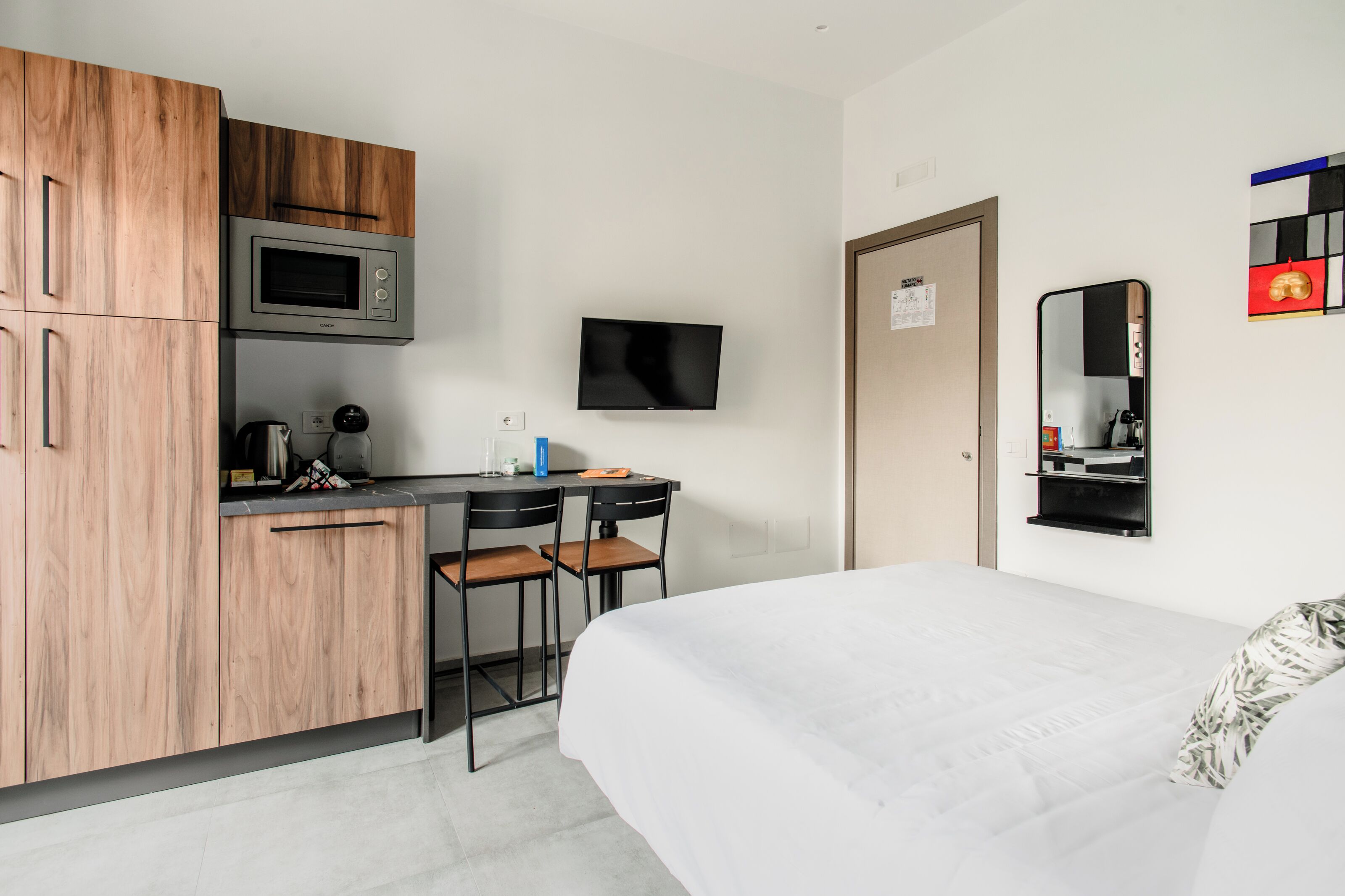 A compact hotel room with a kitchenette, a bed, a TV, and a mirror.