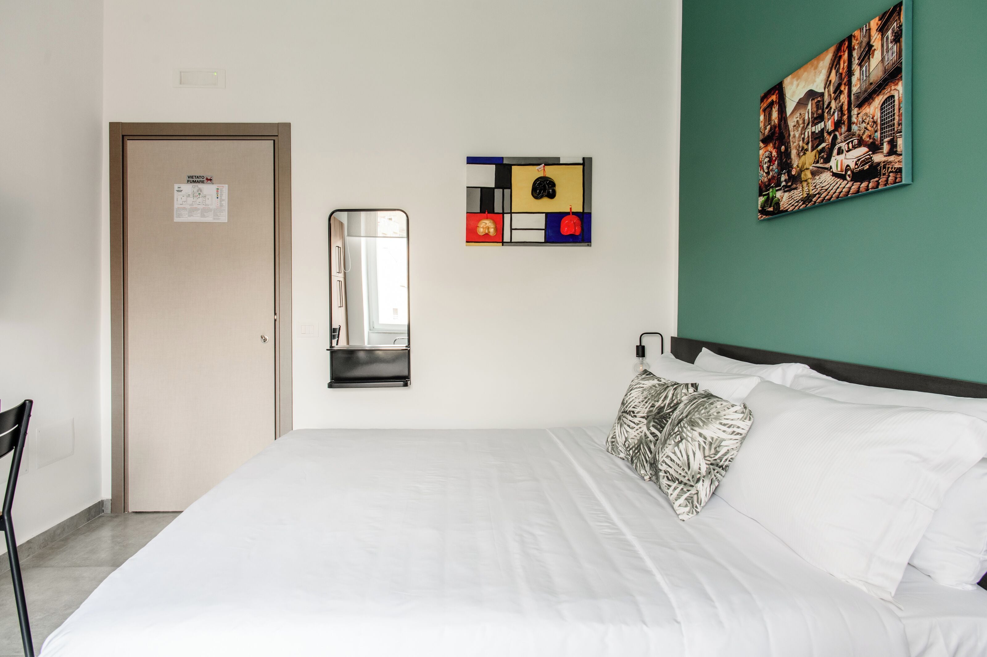 Een hotelkamer met een bed, een spiegel, een kunstwerk aan de muur en een deur.
