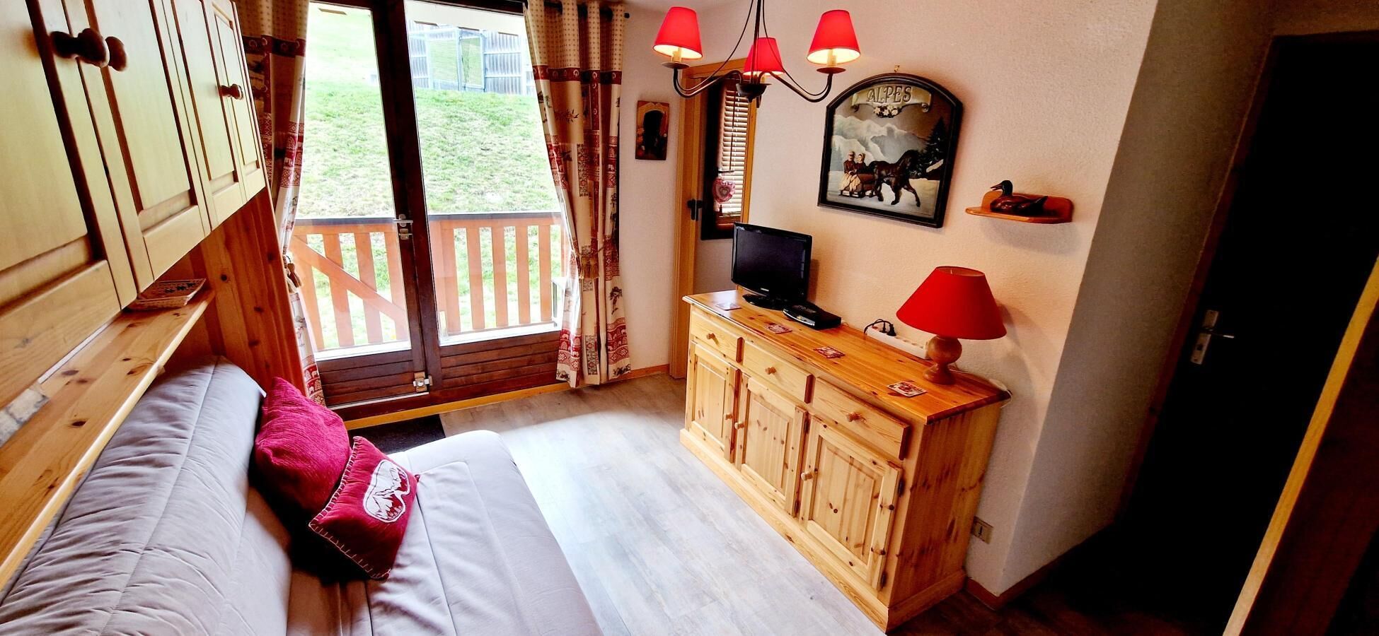 A bedroom with a bed, wooden wardrobe, TV, and a window with curtains.