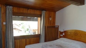 Ein Zimmer mit Holzwänden, einem Bett, Vorhängen und einem Fenster mit Blick auf Gebäude.
