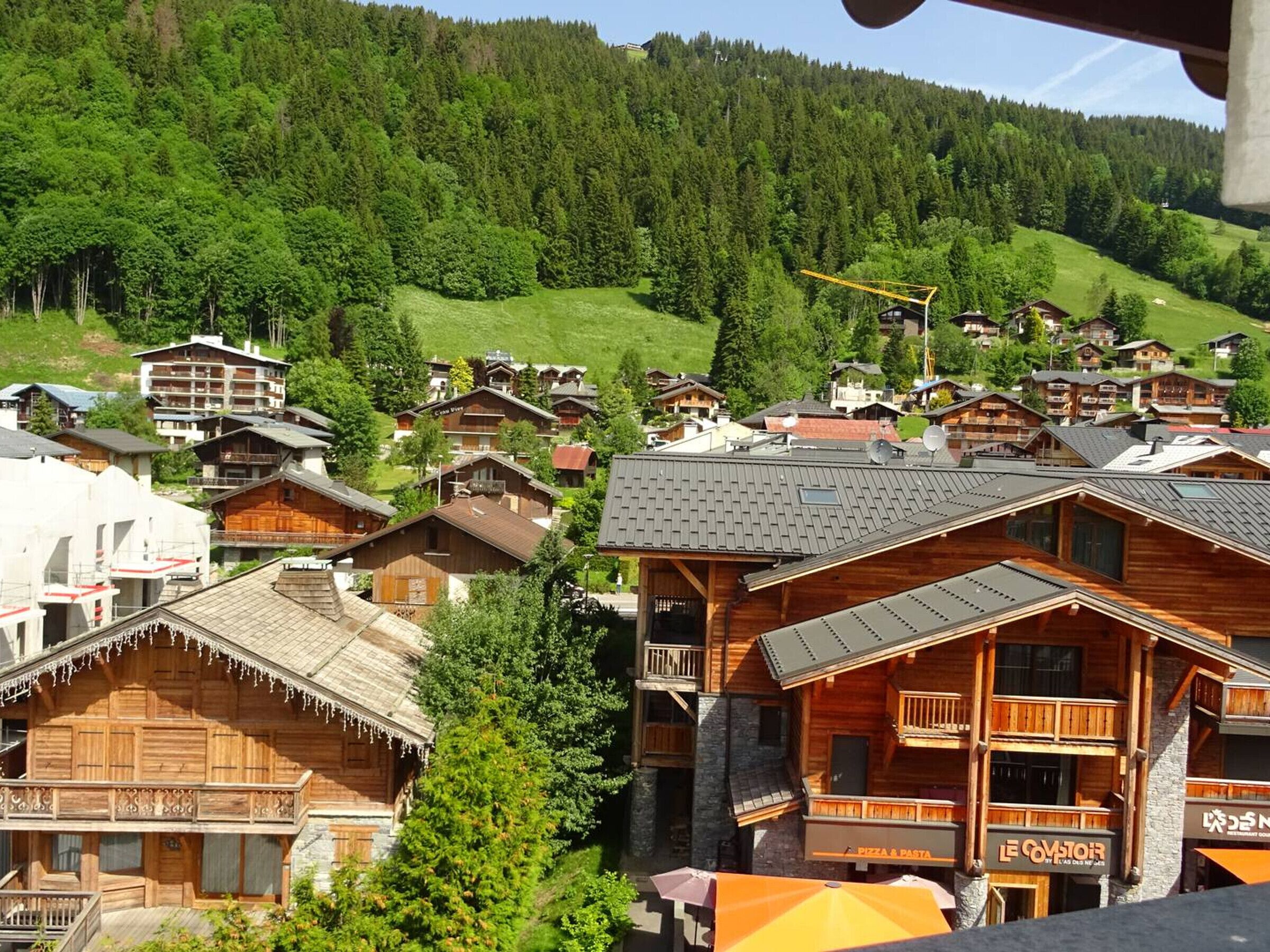 Ein Bergurlaubsort mit Holzhäusern, einem Restaurant für Pizza und Pasta sowie einer Seilbahn im Hintergrund.