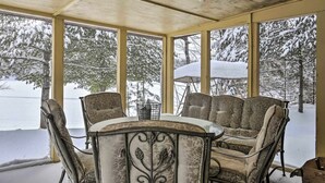 Ein überdachter Außenbereich mit Tisch und Stühlen, großen Fenstern und Blick auf schneebedeckte Bäume.