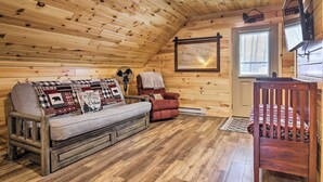 Ein gemütliches Blockhaus-Interieur mit Holzbalkendecke, einer Couch mit gemustertem Überwurf, einem roten Sessel und einem hölzernen Wiege.