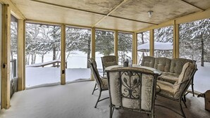 Ein überdachter Außenbereich mit Tisch und Stühlen, großen Fenstern und Blick auf schneebedeckte Bäume.