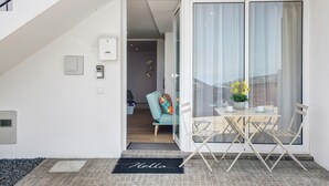 A modern apartment with a staircase, a sliding glass door leading to a balcony, a small dining table with chairs, and a welcome mat.