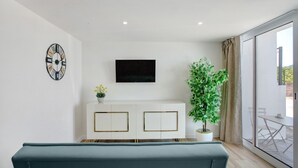 A modern living room with a sofa, a flat-screen TV, a decorative clock, a white cabinet, and a potted plant.