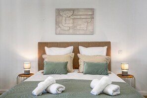 Un lit bien fait, avec une tête de lit, deux tables de chevet avec des lampes et une œuvre d’art accrochée au mur.