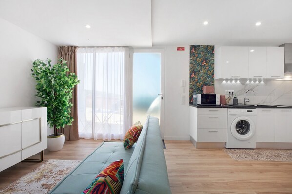 Un appartement moderne comprenant un canapé, une plante en pot, un lave-linge et un coin cuisine.