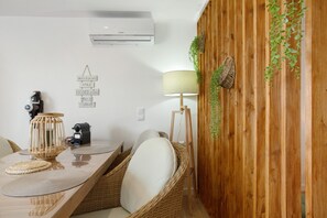 Un coin repas avec des chaises en osier, une table avec des sets de table, une lampe et un climatiseur fixé au mur.