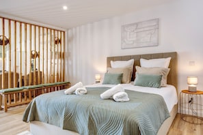 Een hotelkamer met een bed, nachtkastjes, een aan de muur hangend kunstwerk en een houten scheidingswand met hangmanden.