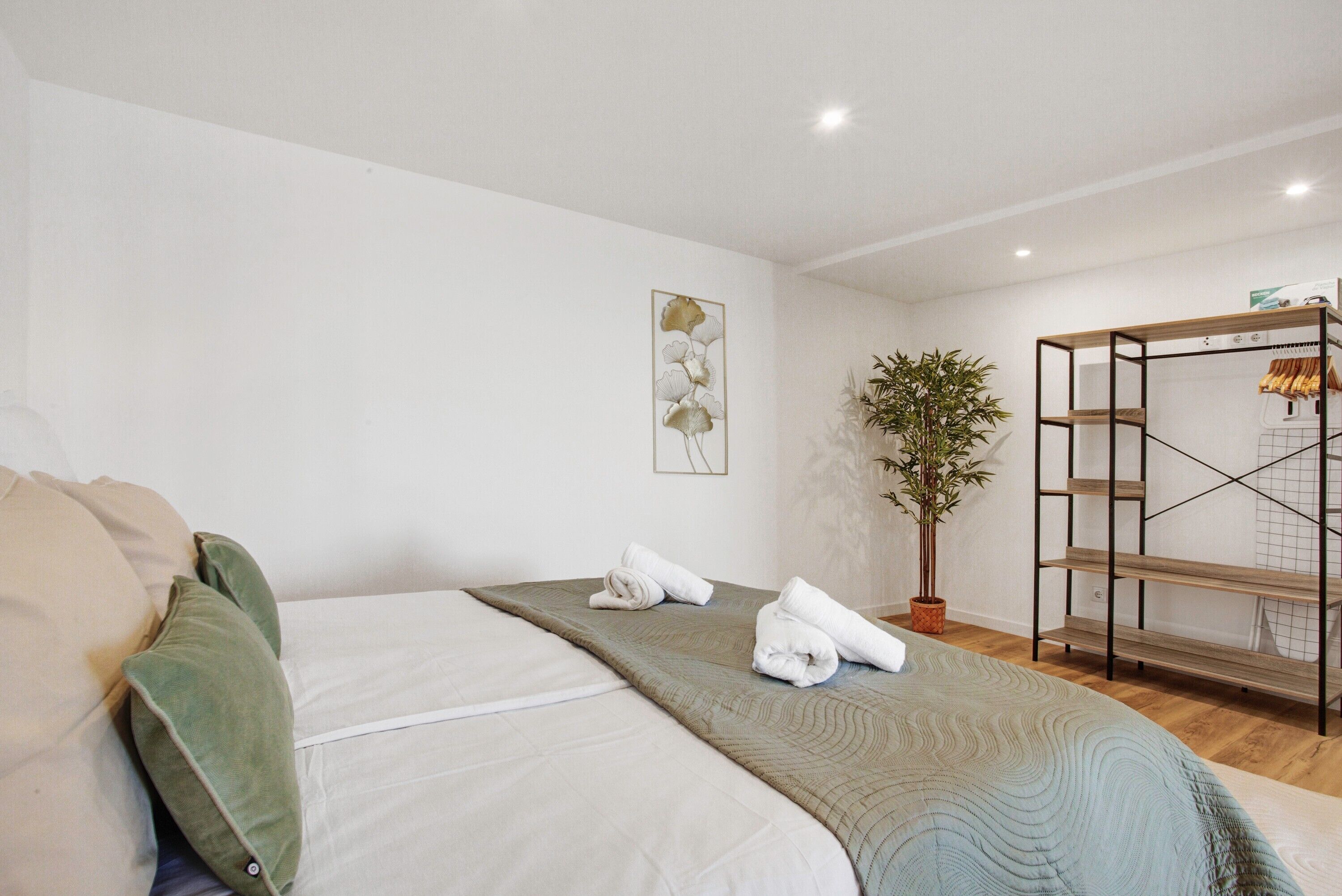 Ein Hotelzimmer mit einem Bett, einer Zimmerpflanze, einem Holzboden und einem gerahmten Kunstwerk an der Wand.