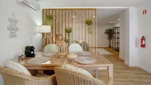 A dining area with a wooden table, wicker chairs, a coffee machine, and a decorative partition with hanging plants.