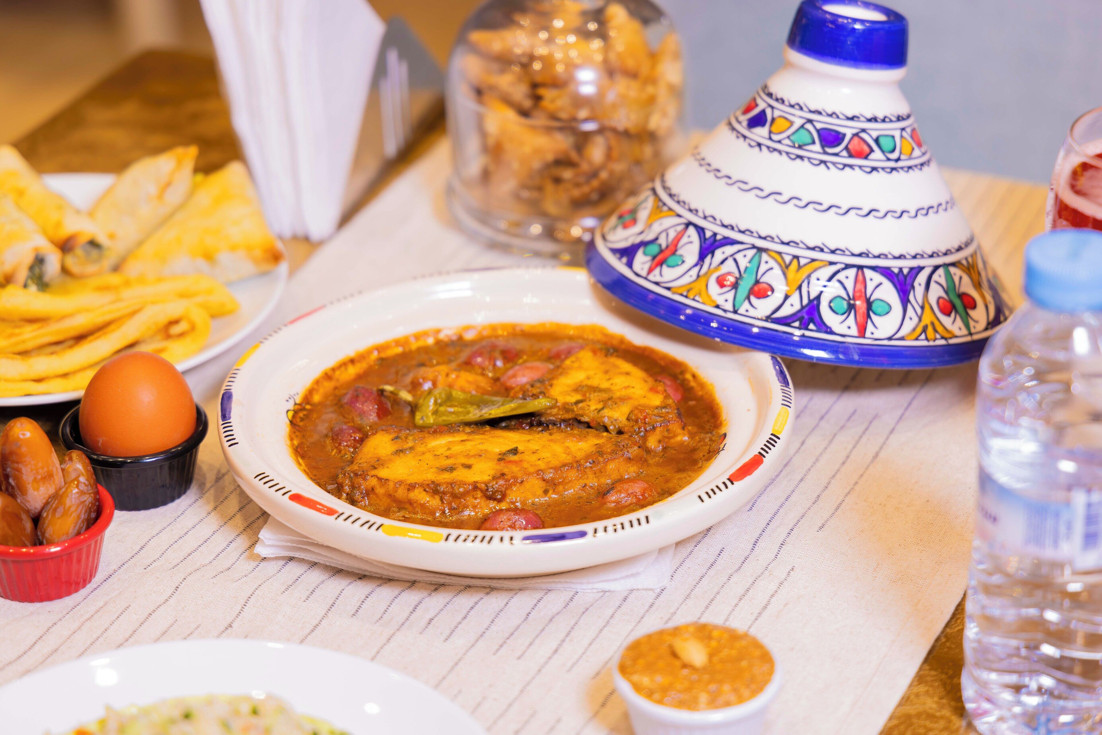 A dining table with various dishes, including a fish dish, a bowl of olives, and a decorative pot.