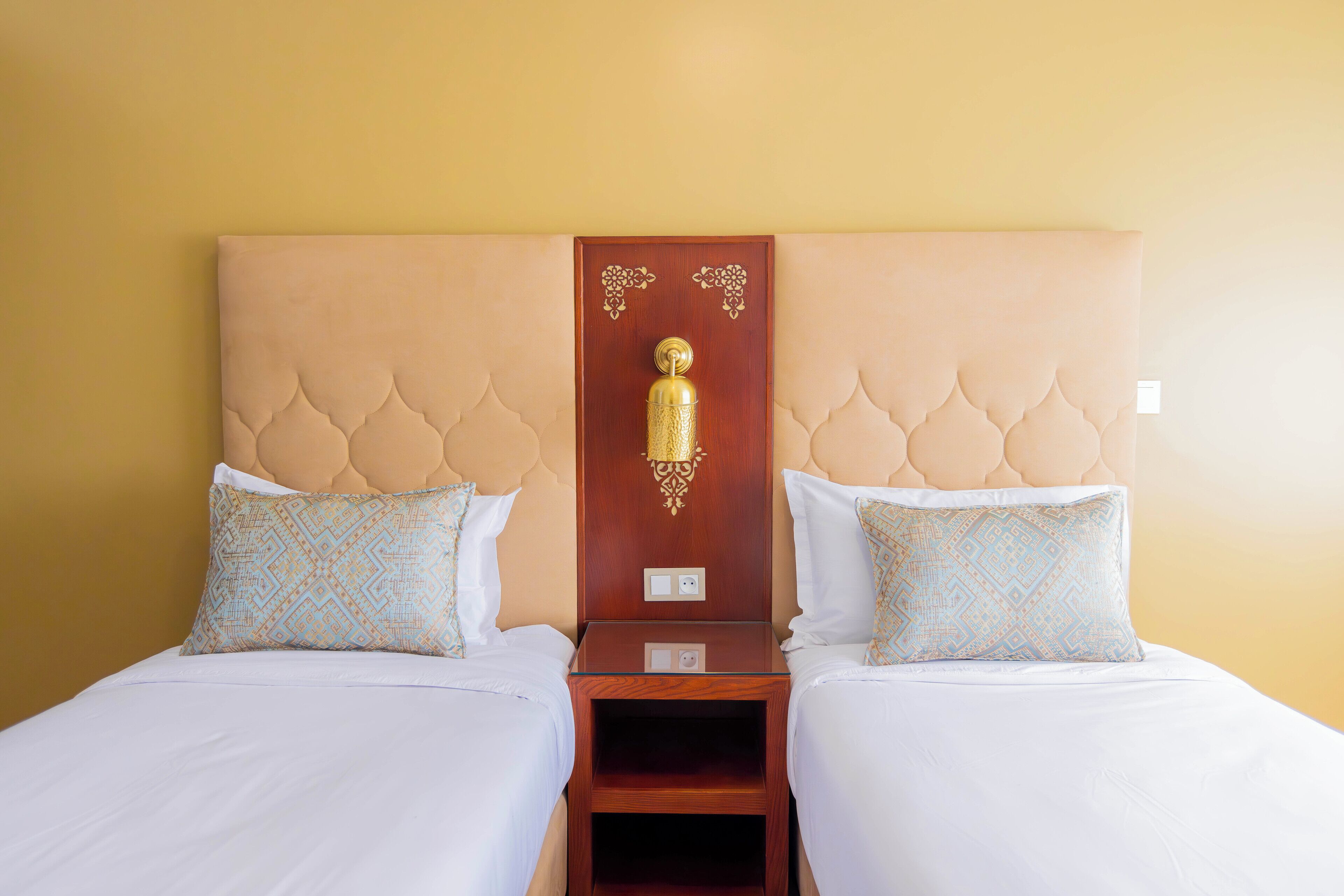 A double bed with a tufted headboard, two matching pillows, and a nightstand with a lamp.