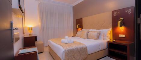 Habitación de hotel con una cama grande, mesitas de noche, un espejo y una lámpara en el techo.