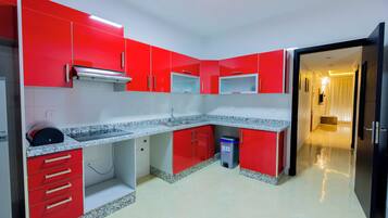 A kitchen with red cabinets, granite countertops, and a trash bin.