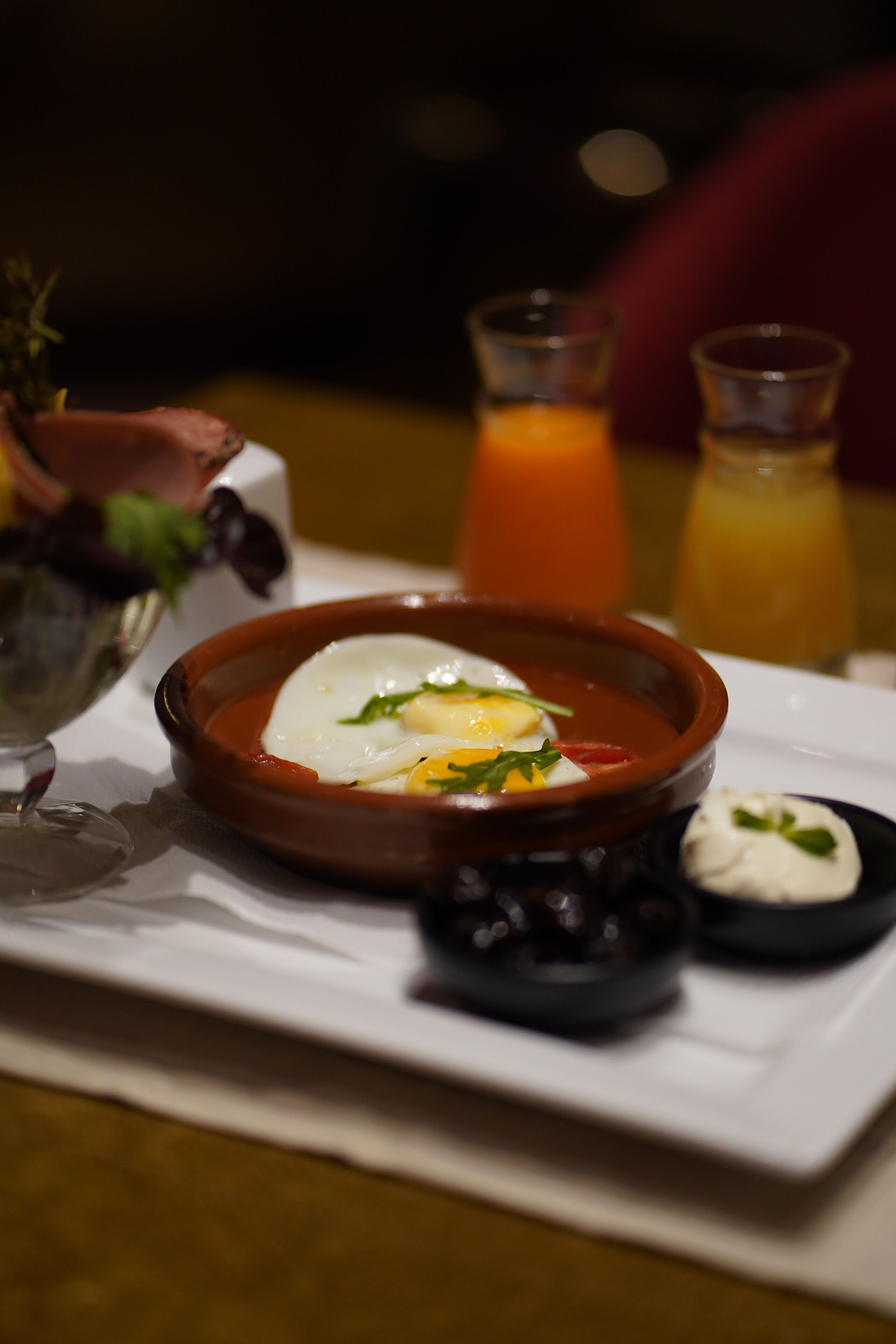 Uma mesa de jantar com uma tigela de sopa, um copo de suco de laranja e um pequeno prato de creme.