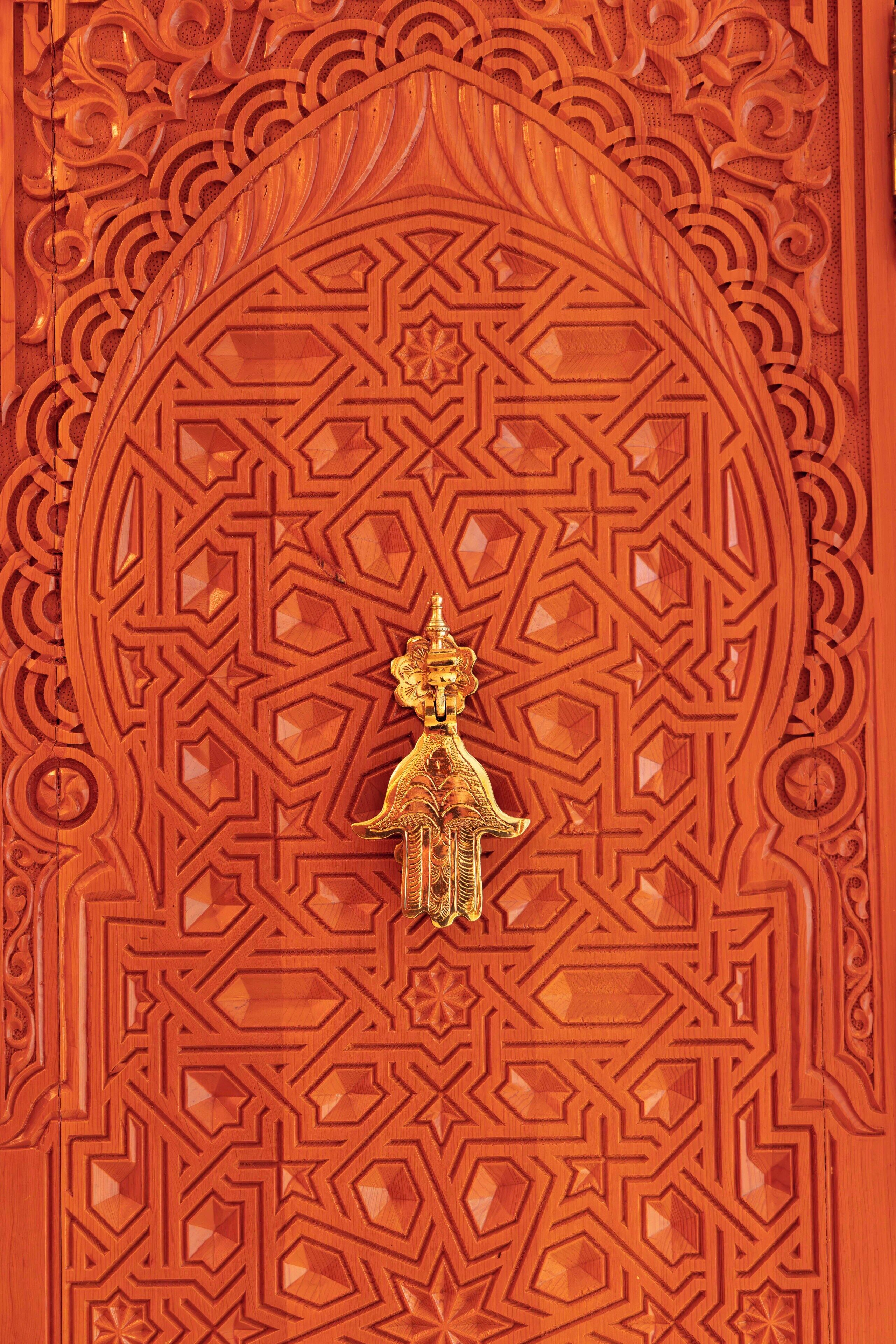 A detailed carved wooden door with geometric patterns and a central golden figure.
