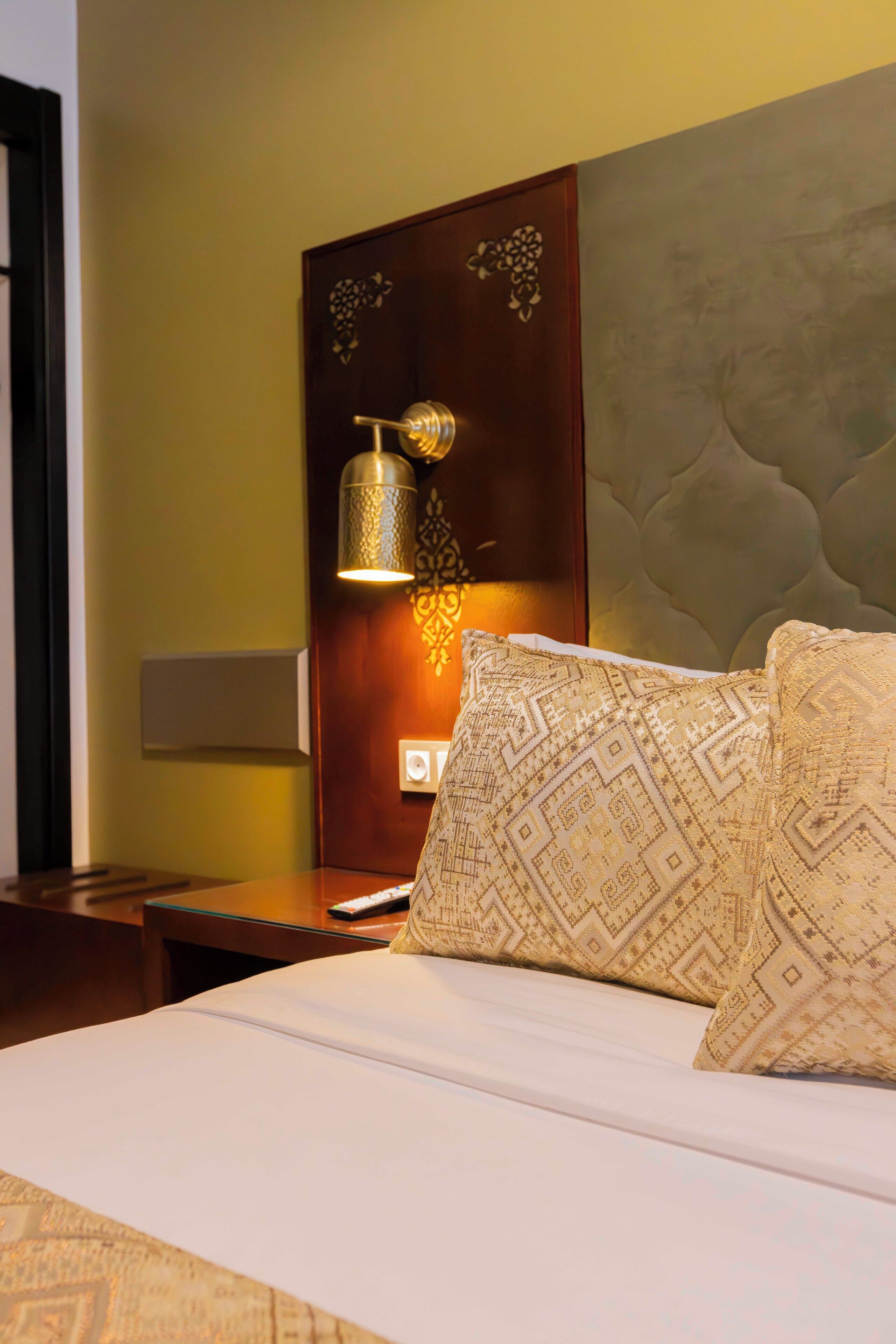 A hotel room with a neatly made bed, a bedside lamp, and a wall-mounted light fixture.