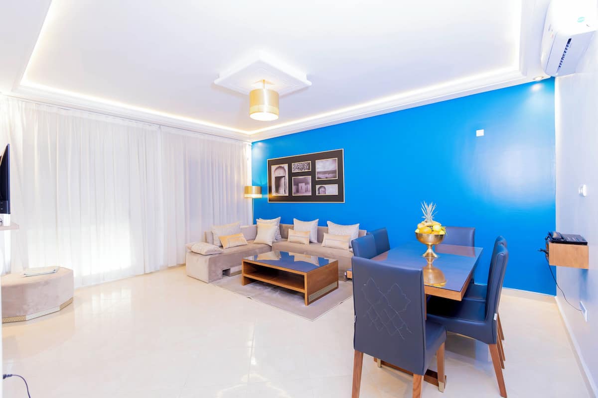 Una sala de estar moderna con una pared azul de acento, un sofá seccional, una mesa de centro y una zona de comedor con sillas.