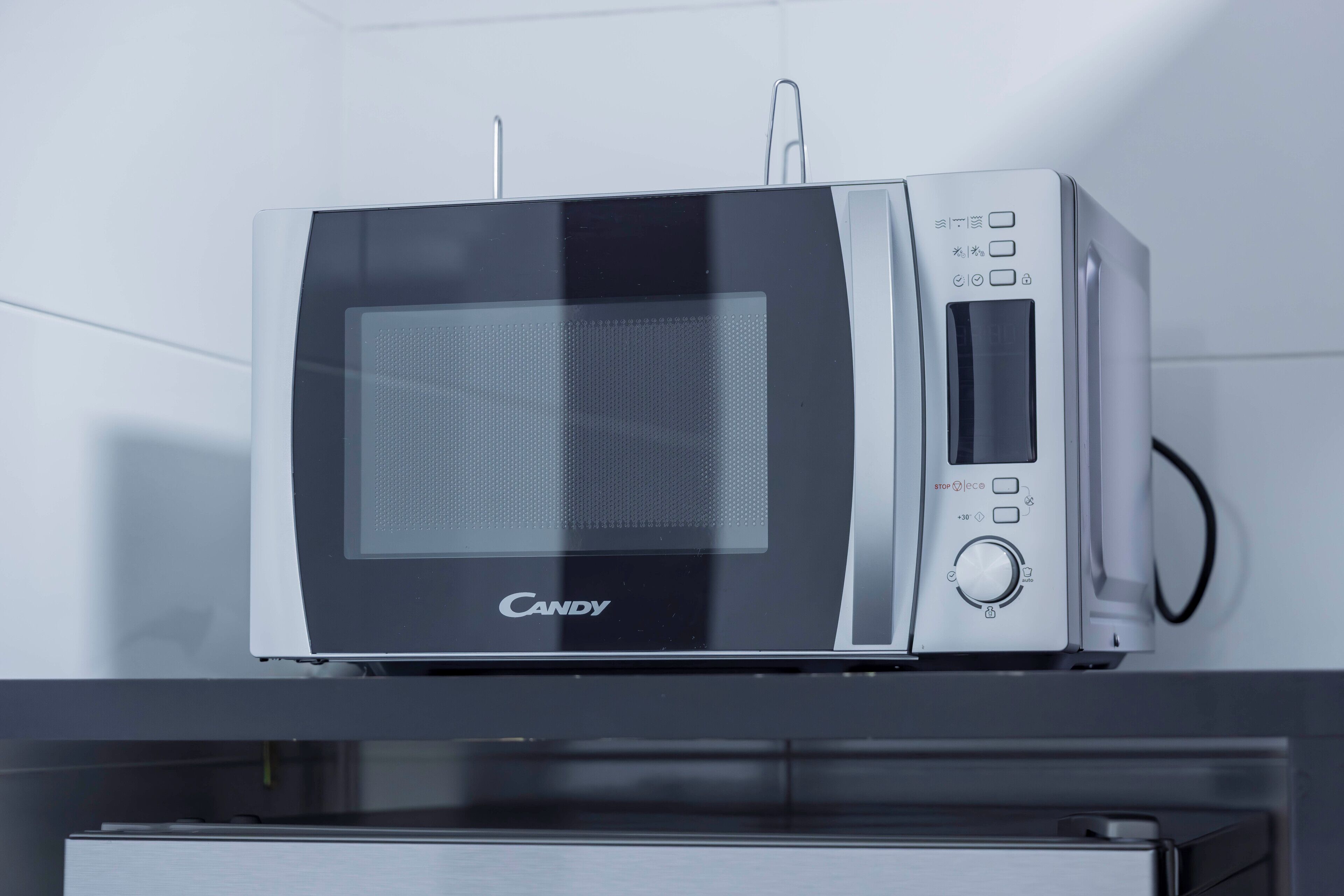 Un horno microondas con pantalla digital y panel de control, colocado en un estante.