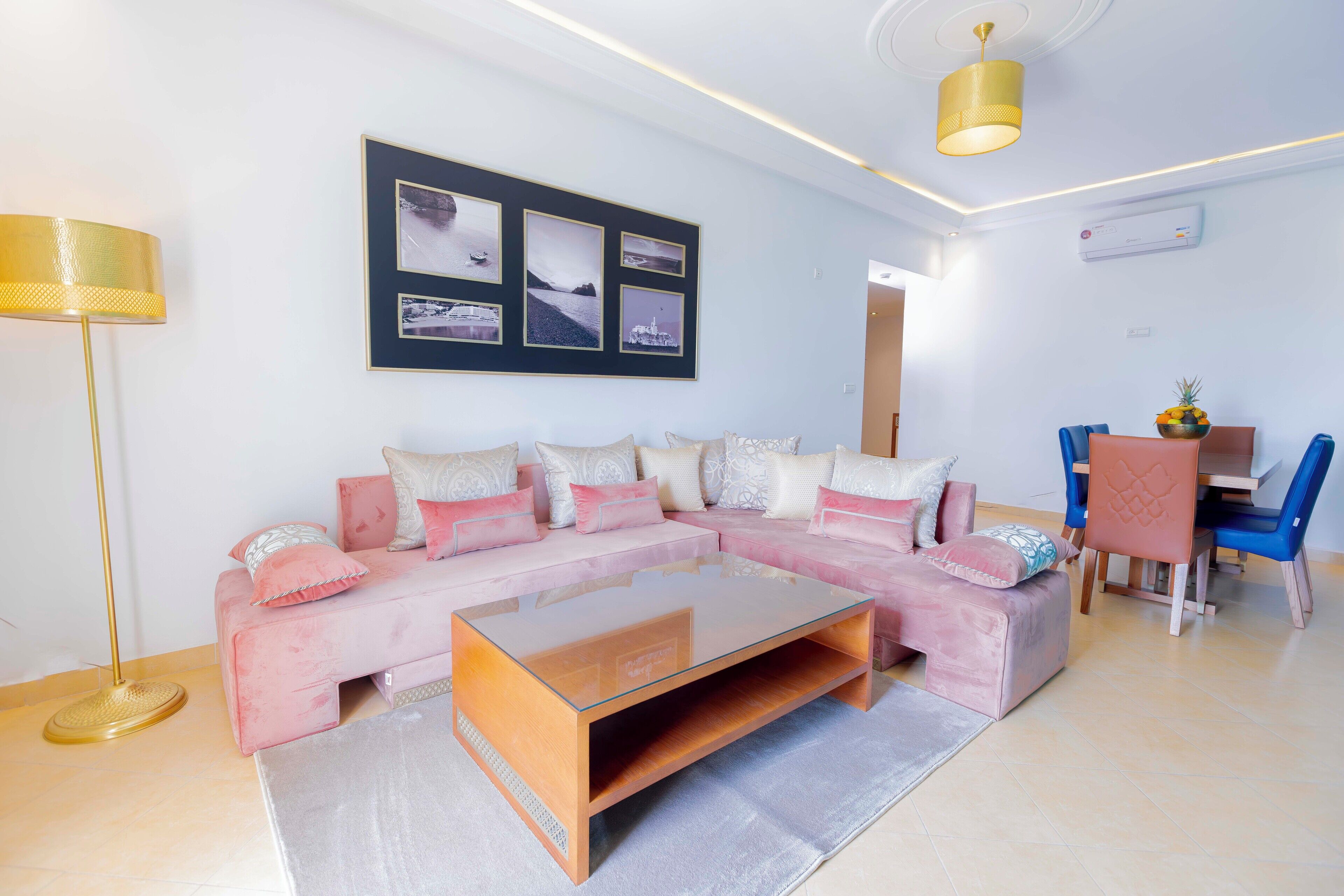Una sala de estar moderna con un sofá seccional rosa, una mesa de centro de vidrio y un comedor con sillas azules.