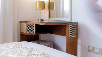 A hotel room with a bed, a wooden desk with a lamp, a mirror, and a patterned bedspread.