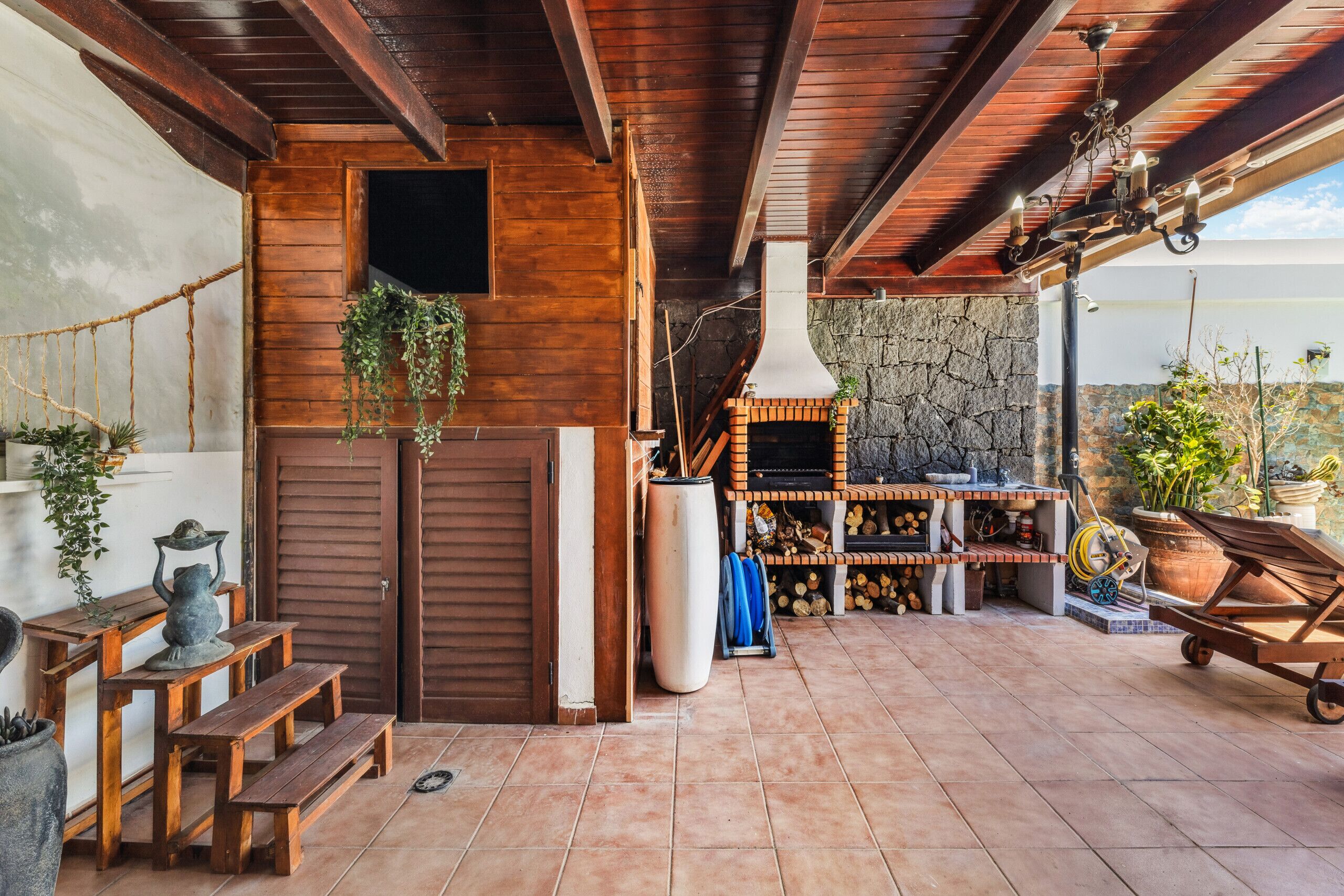 A covered patio area with wooden benches, a stone wall, and a grill.