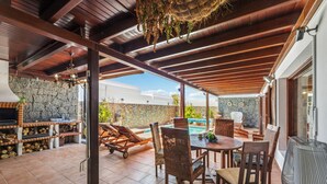 Un patio exterior con muro de piedra, muebles de madera y piscina.