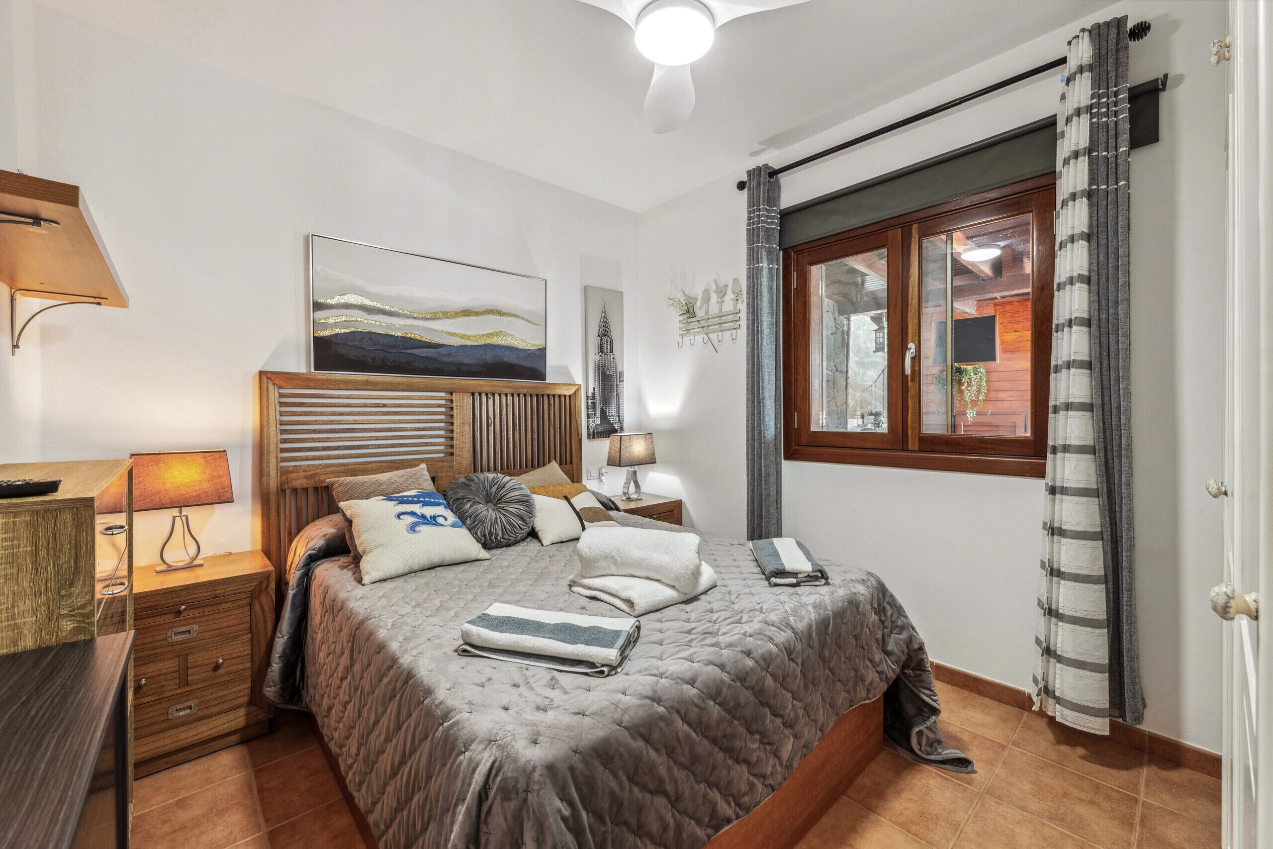Une chambre bien rangée, avec un lit, des tables de chevet, une lampe et une fenêtre avec des rideaux.