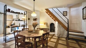 Un espace repas avec une table ronde en bois et des chaises, un luminaire suspendu et un escalier menant à un niveau supérieur.