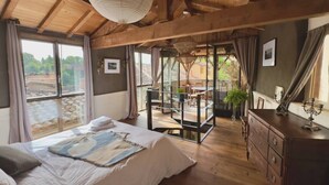 Une chambre spacieuse avec un grand lit, un plancher en bois et un balcon équipé d’une table et de chaises.