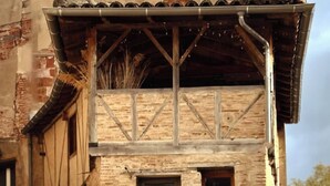 Un bâtiment doté d’un balcon en bois soutenu par des poutres métalliques, d’une façade en briques et d’une fenêtre avec une porte.