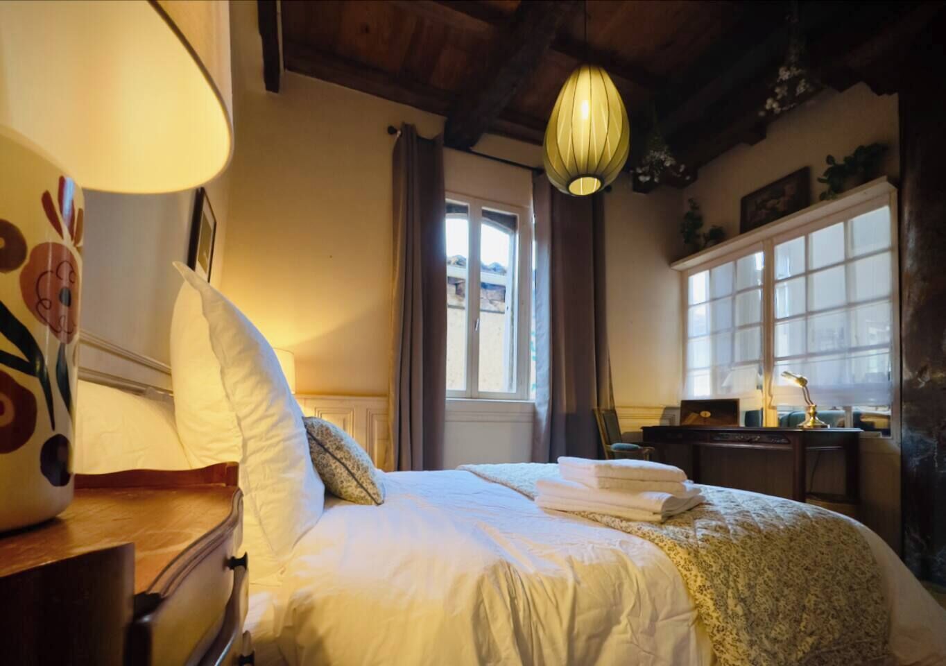 Ett mysigt sovrum med en säng, ett skrivbord, en lampa och ett fönster med gardiner.