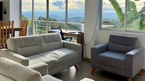 Un salon moderne avec de grandes fenêtres, un bureau et deux canapés gris.