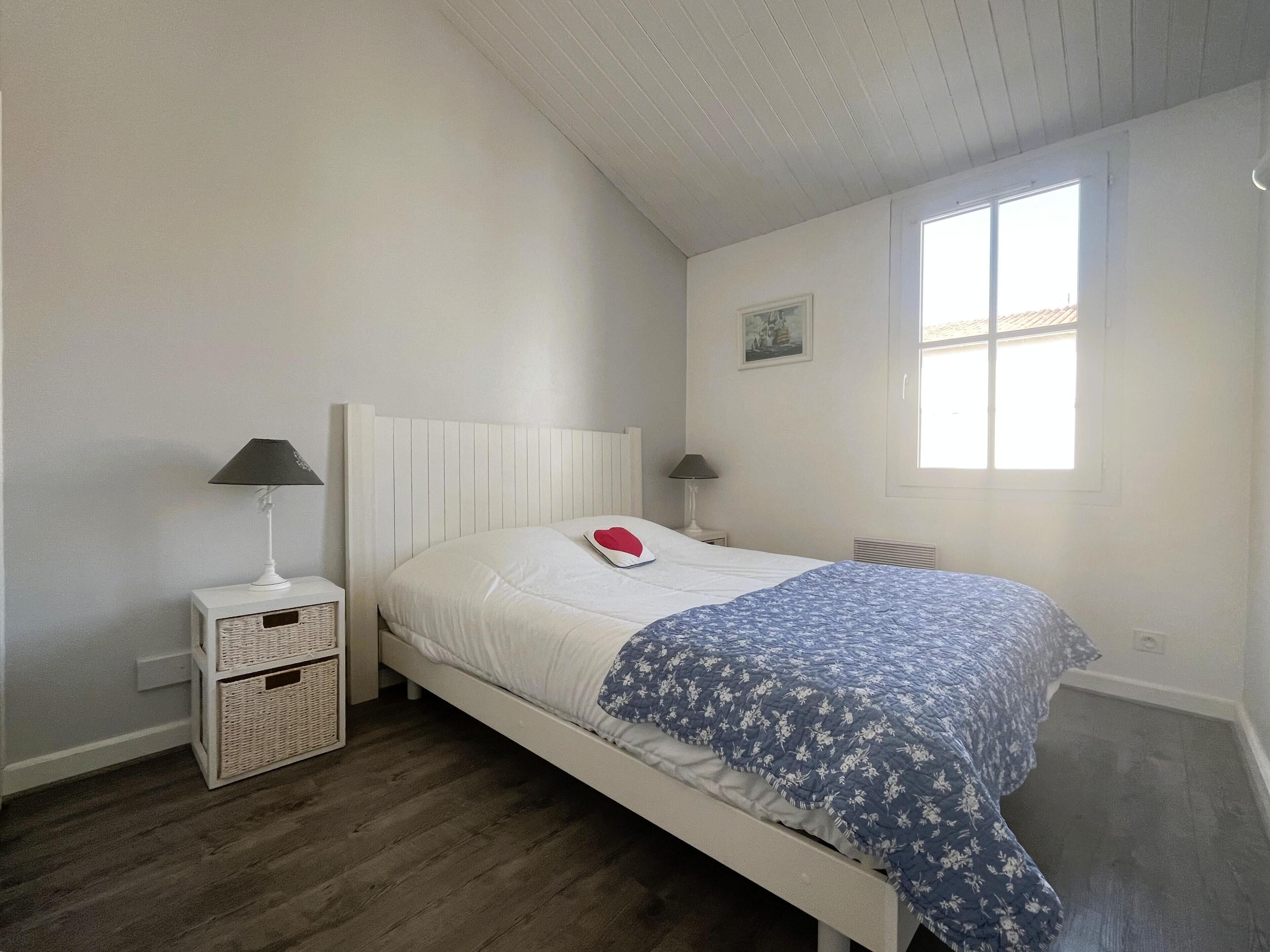 Une chambre à coucher avec un lit blanc, une couvre-lit à motifs floraux bleus, deux lampes de chevet et une fenêtre.