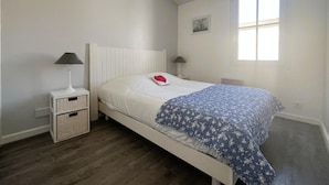 A bedroom with a white bed, a blue floral bedspread, two bedside lamps, and a window.